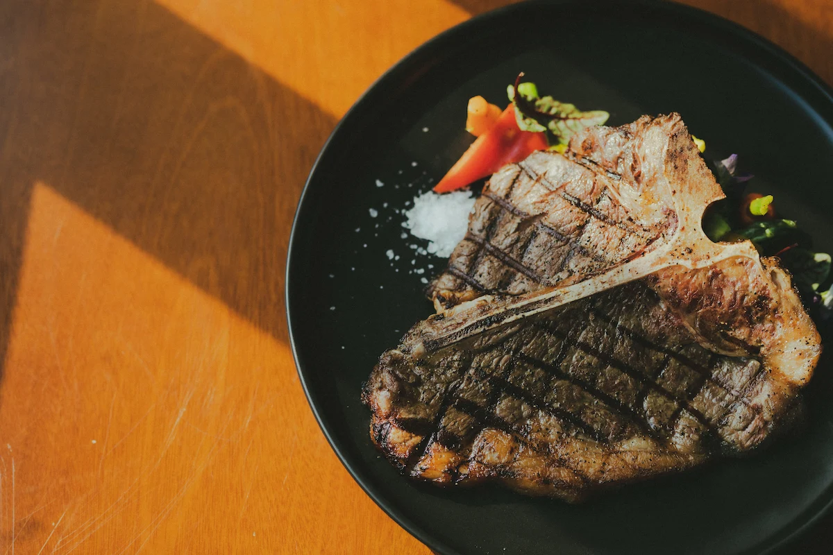 T-Bone Steak mit Knochen, kräftiger Kruste angerichtetauf einem schwarzen Teller, angebraten und servierfertig angerichtet