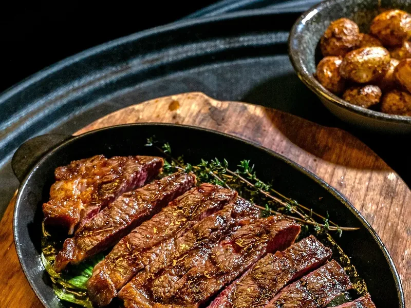 Aufgeschnittenes medium-rare Steak in einer Gusseisenpfanne mit Thymian auf Holzbrett